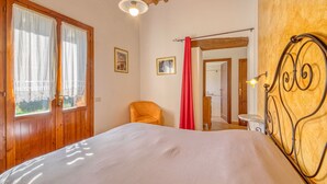 Une chambre avec une porte en bois, un lit avec une tête de lit en métal, une chaise et un rideau rouge.