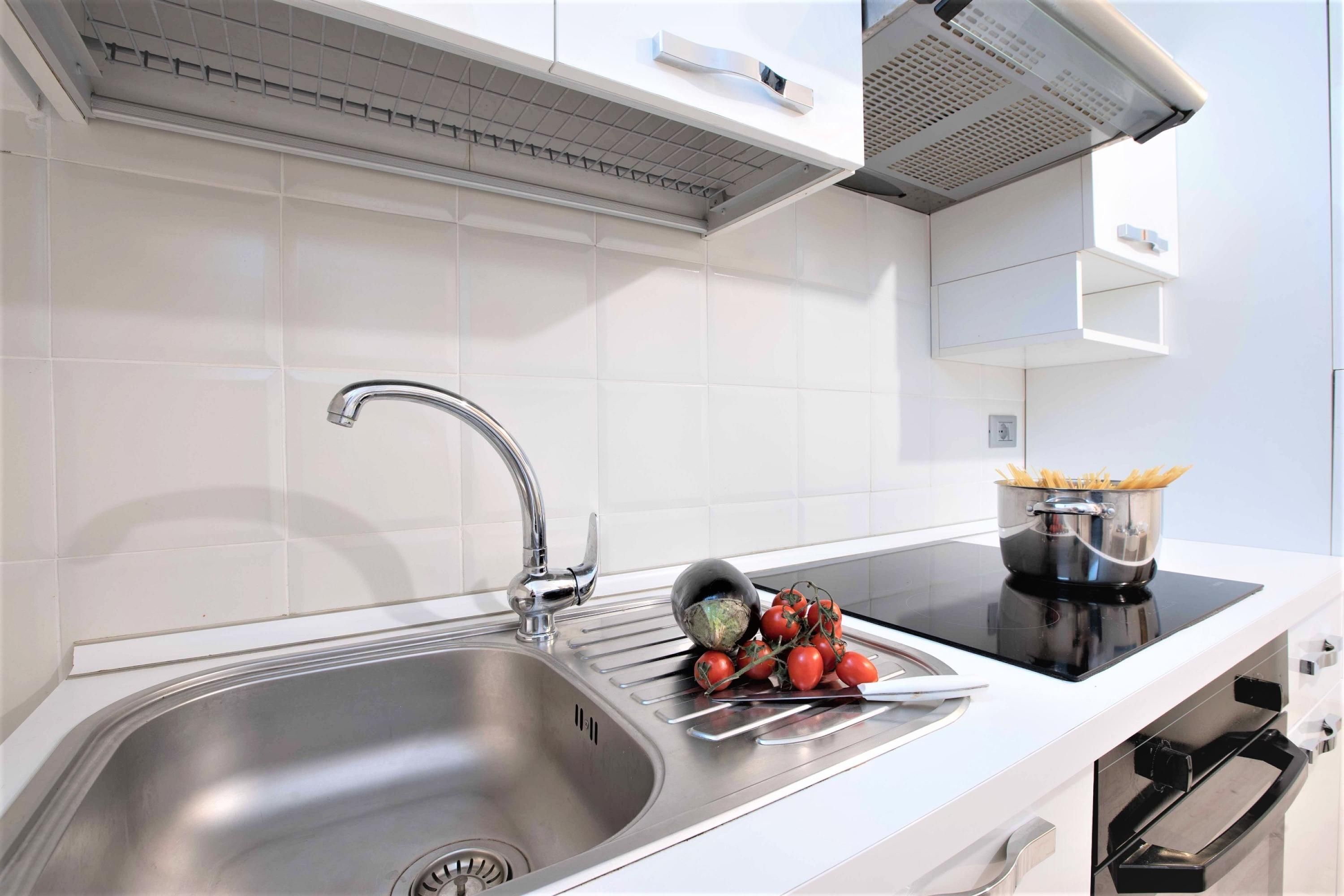 A modern kitchen with a stainless steel sink, a black induction cooktop, and a built-in oven.