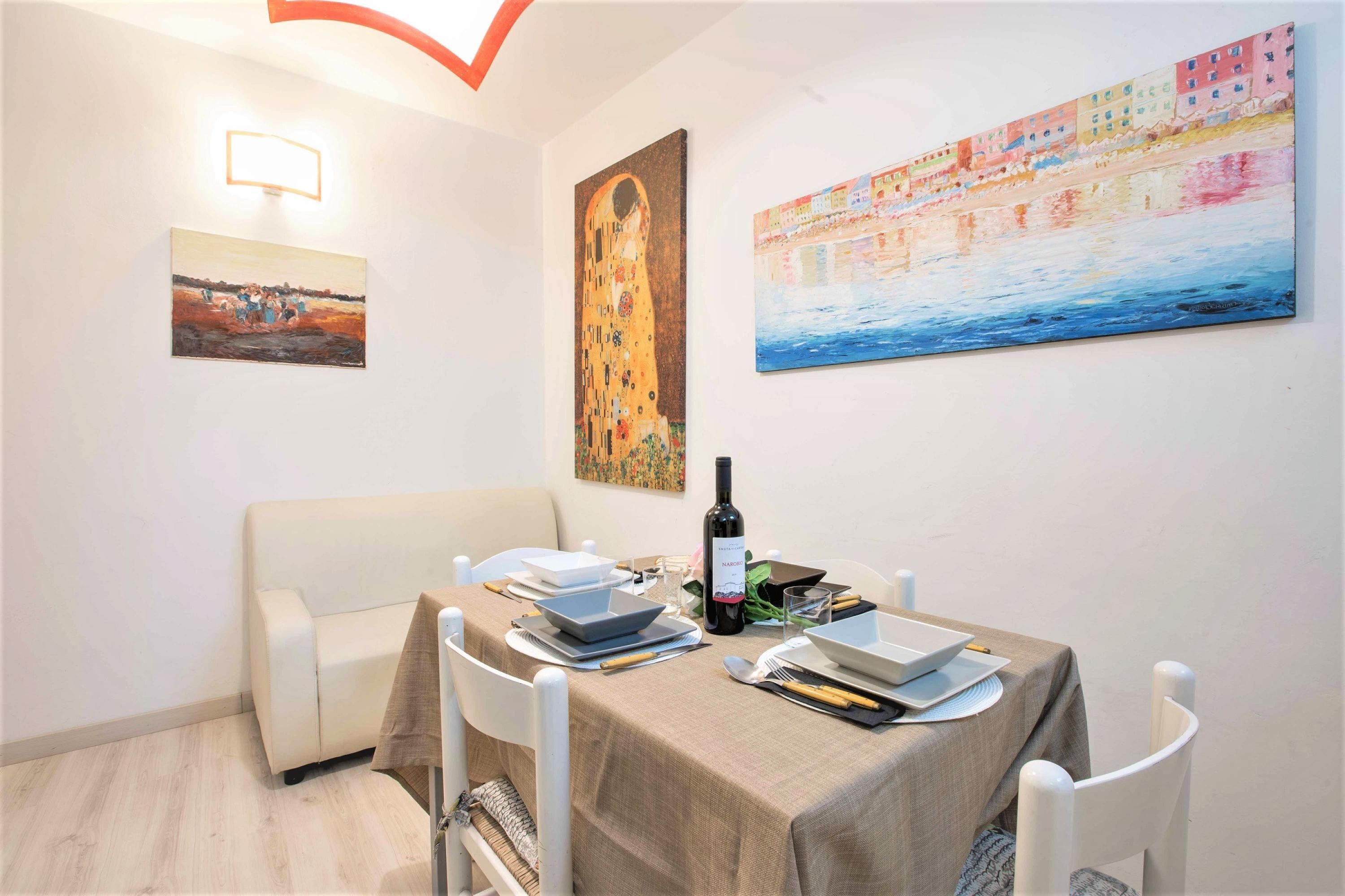A dining area with a table set for two, a sofa, and wall art including a famous painting and a landscape.