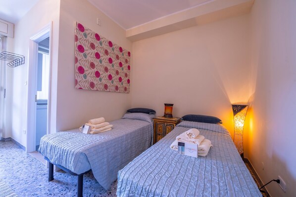 Une chambre d’hôtel avec deux lits simples, une petite table de chevet en bois, une œuvre d’art accrochée au mur et une lampe de chevet.