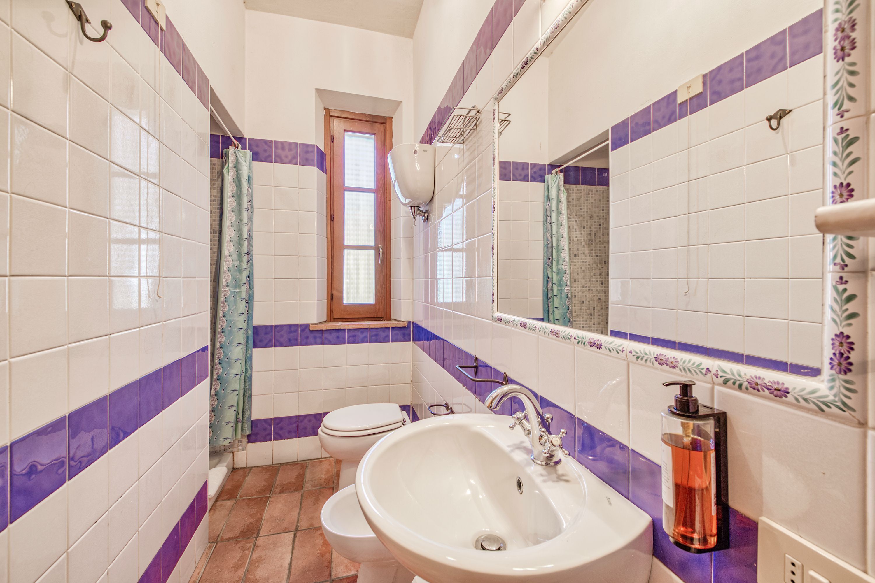 Une salle de bain avec des carreaux blancs et violets, un lavabo blanc, des toilettes et une fenêtre.