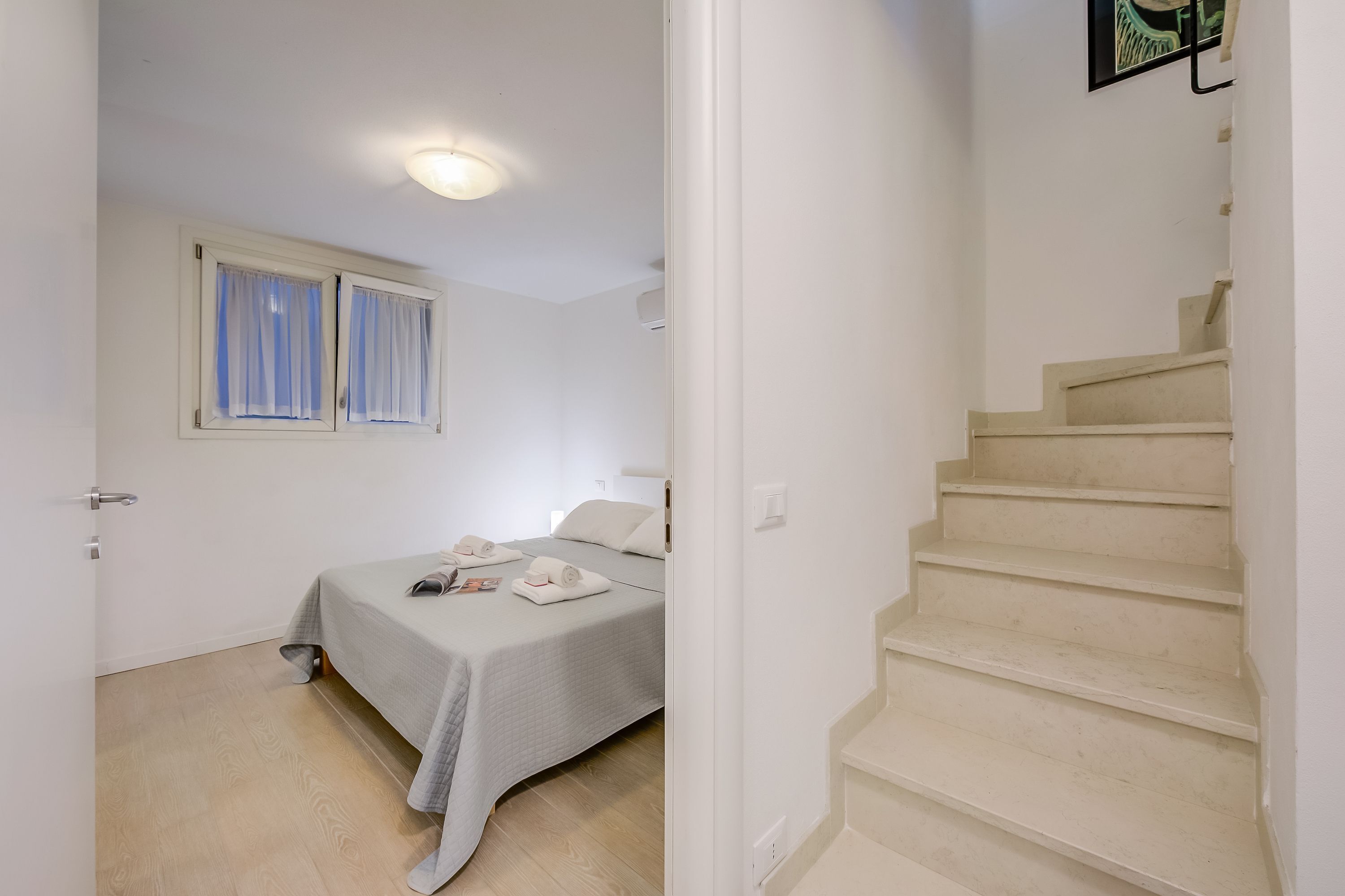 A bedroom with a bed, a bedside table, a window with curtains, and a staircase.