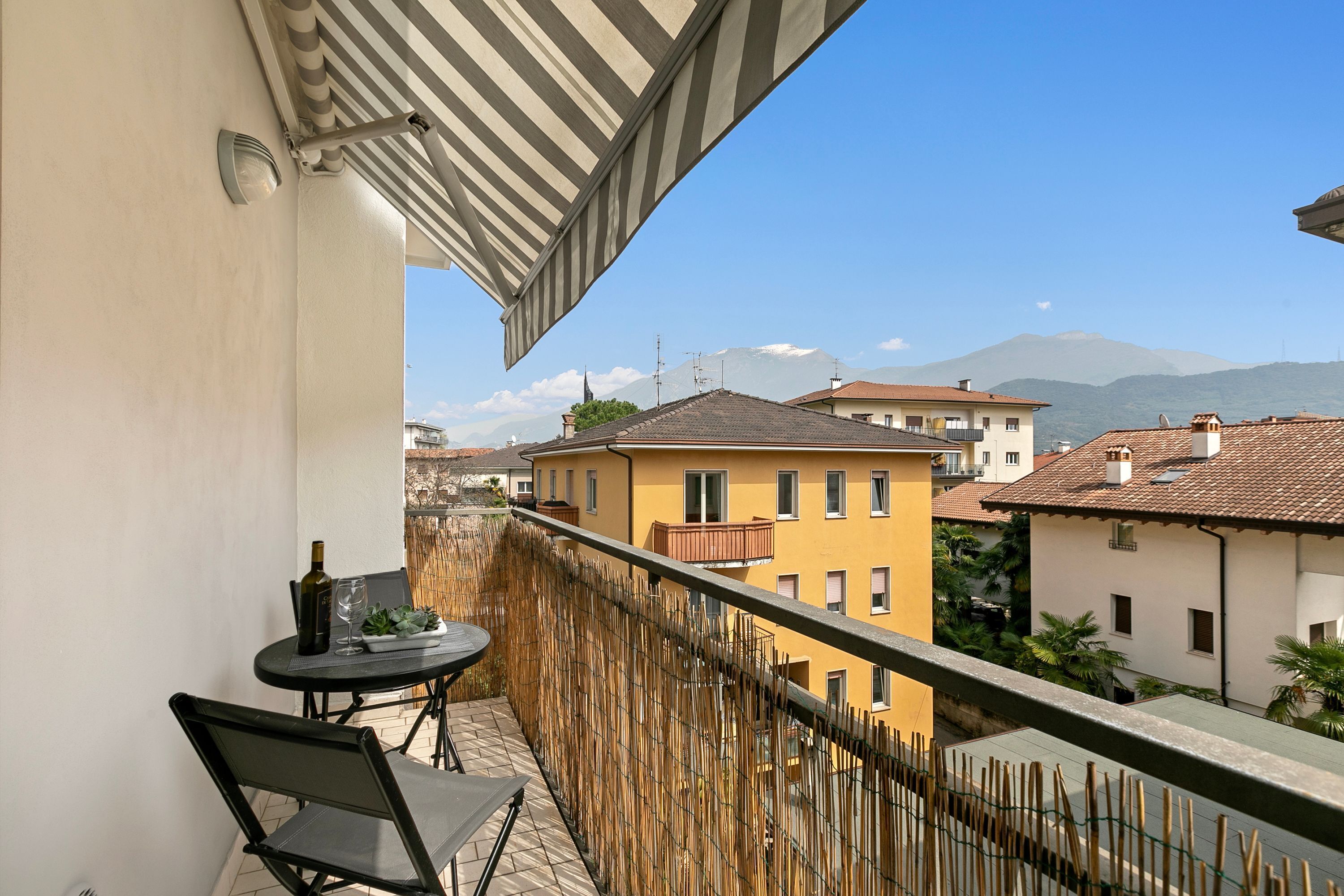 A balcony with a table and chairs, overlooking a residential area with buildings and mountains in the background.