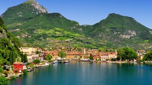 Une ville côtière, avec une montagne imposante en arrière-plan, un port où sont amarrés des bateaux et des bâtiments à l’architecture traditionnelle.