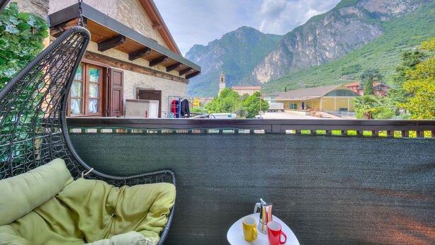 Ein Balkon mit einem Korbstuhl und einem Tisch mit zwei Tassen, mit Blick auf einen Berg und ein Gebäude mit einem Glockenturm.
