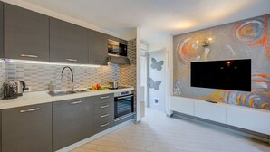 Eine moderne Küche mit grauen Schränken, einem eingebauten Backofen und einem großen Fernseher an der Wand.