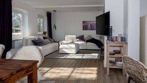 A modern living room with a white sofa, a wooden coffee table, and a television on a wooden stand.