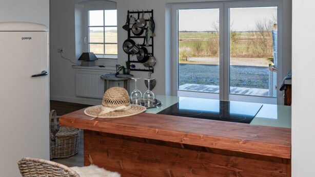 A kitchen with a wooden counter, a refrigerator, a window with a view of the outdoors, and a pot rack.
