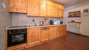 Cocina con armarios de madera, horno empotrado, lavavajillas, microondas y un pequeño estante con adornos.