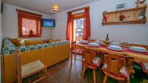 Un comedor acogedor con una mesa de madera dispuesta para cuatro, un sofá con cojines estampados y un televisor montado en la pared.