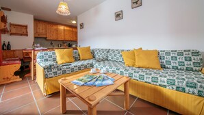 Un área de estar acogedora con un conjunto de sofás, una mesa de centro de madera y una cocina al fondo.