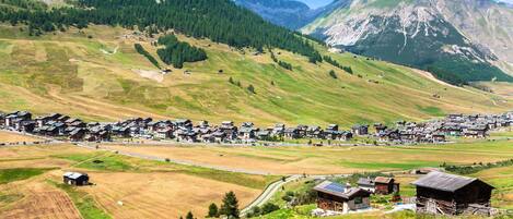 Un village rural, avec des maisons et des granges, entouré de montagnes et de champs.