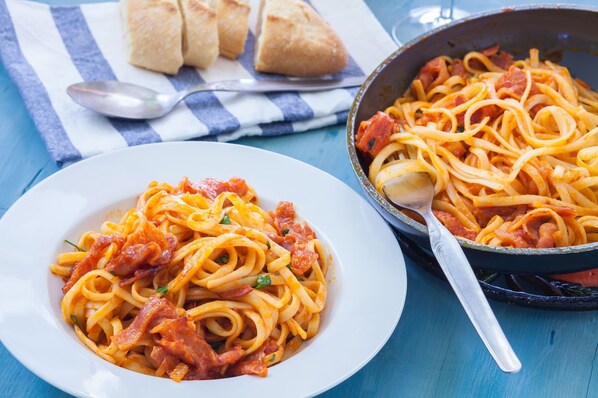 Une assiette de spaghettis à la sauce tomate et aux lardons, et une autre portion de spaghettis dans une poêle.