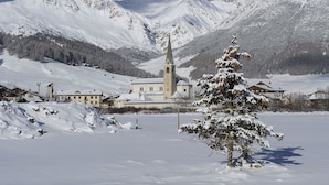 A snow-covered landscape with a church, mountains, and a snow-laden tree. - Volga in Livigno With 2 Bedrooms and 1 Bathrooms (Livigno)