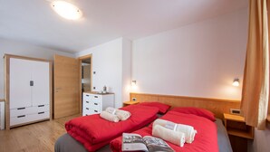 A hotel room with two beds, wooden headboards, a wardrobe, a bedside table with a lamp, and a mirror.