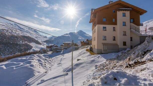 A multi-story building with a ski lift in the background, surrounded by snow-covered mountains.