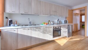 A modern kitchen with light wood cabinets, a stainless steel sink, a built-in oven, and a microwave.