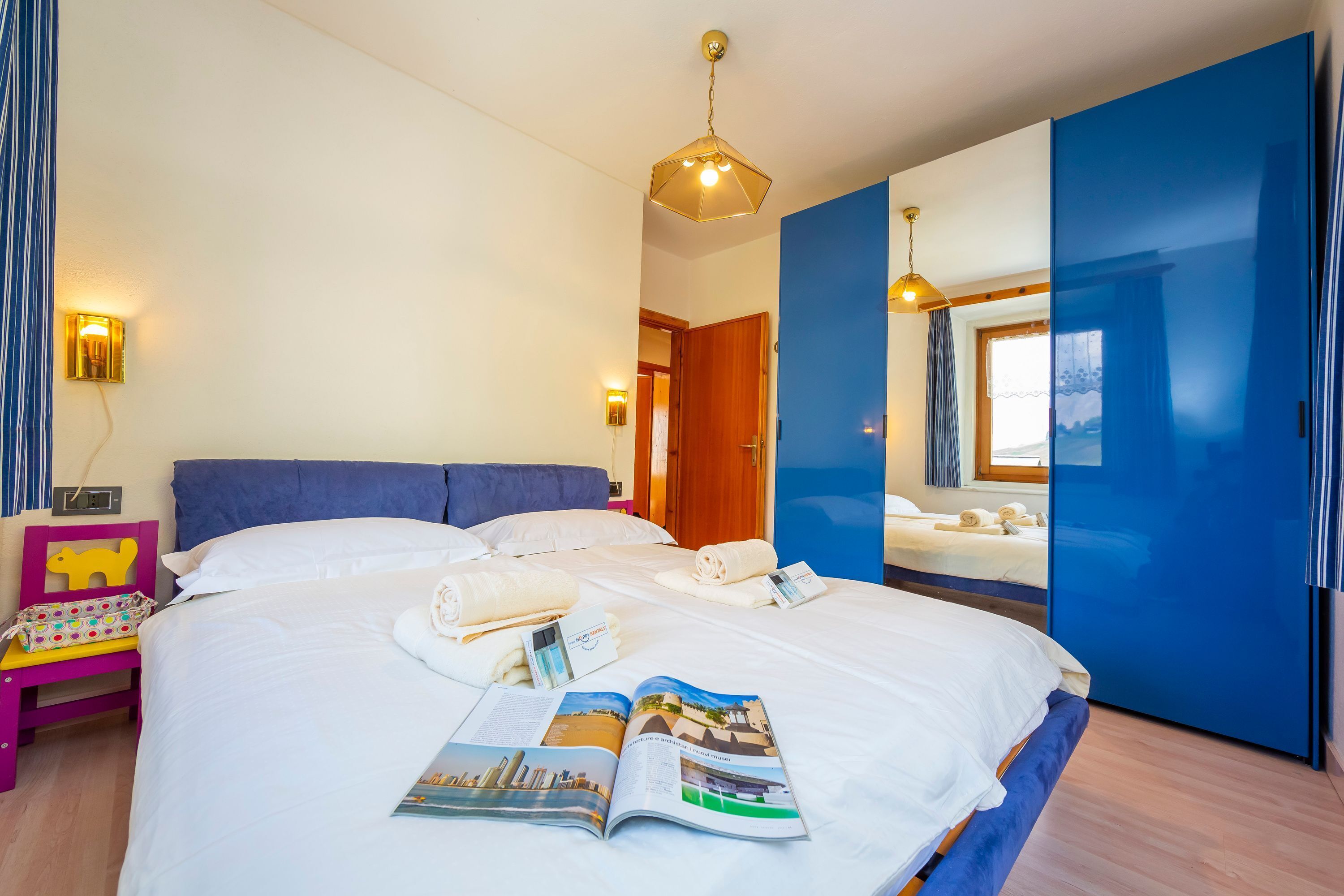Habitación de hotel con una cama grande, una mesita de noche con lámpara, un espejo y vistas al exterior.