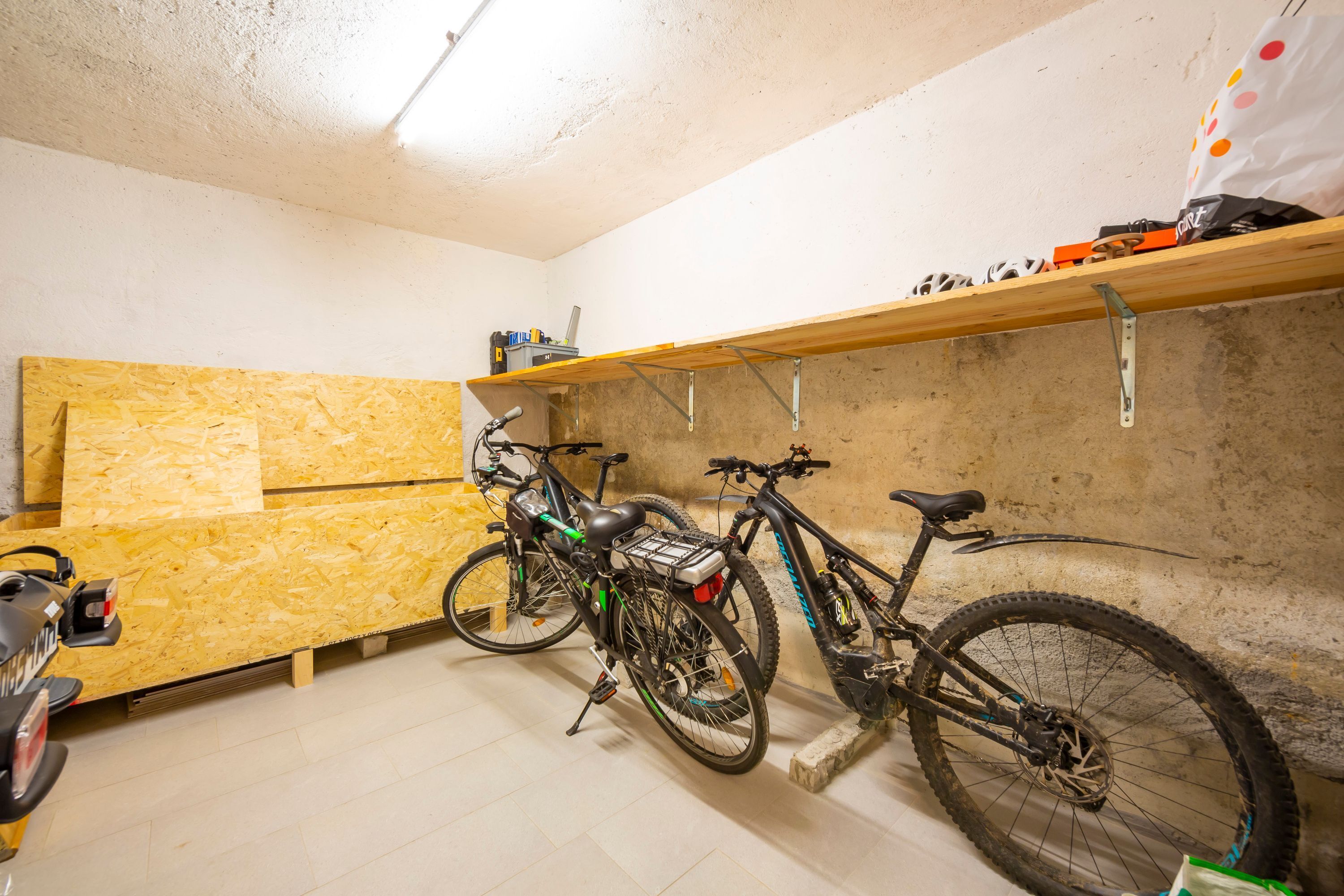 A room with a wooden floor, a bike rack, and a shelf with various items.