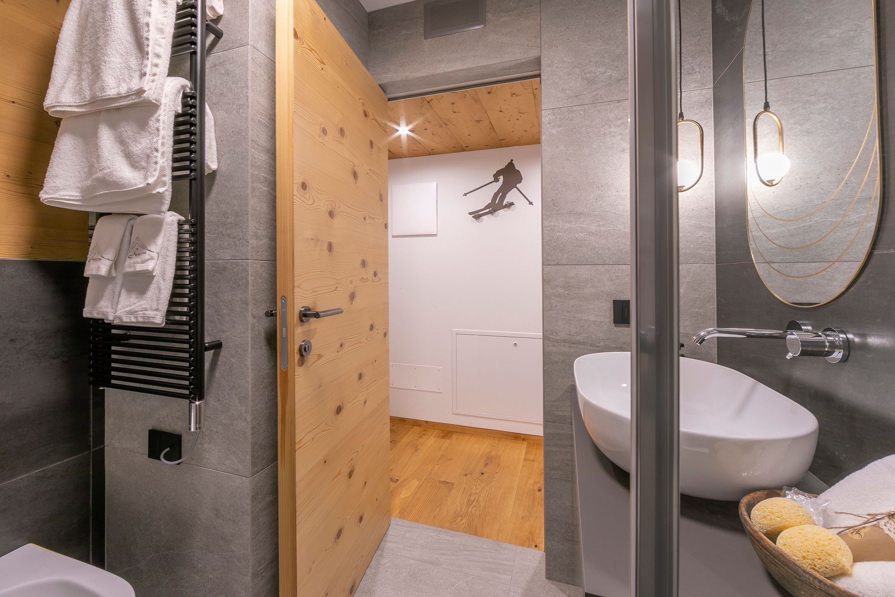 A modern bathroom with a wooden floor, a glass shower enclosure, a white sink, and a towel rack with multiple towels.