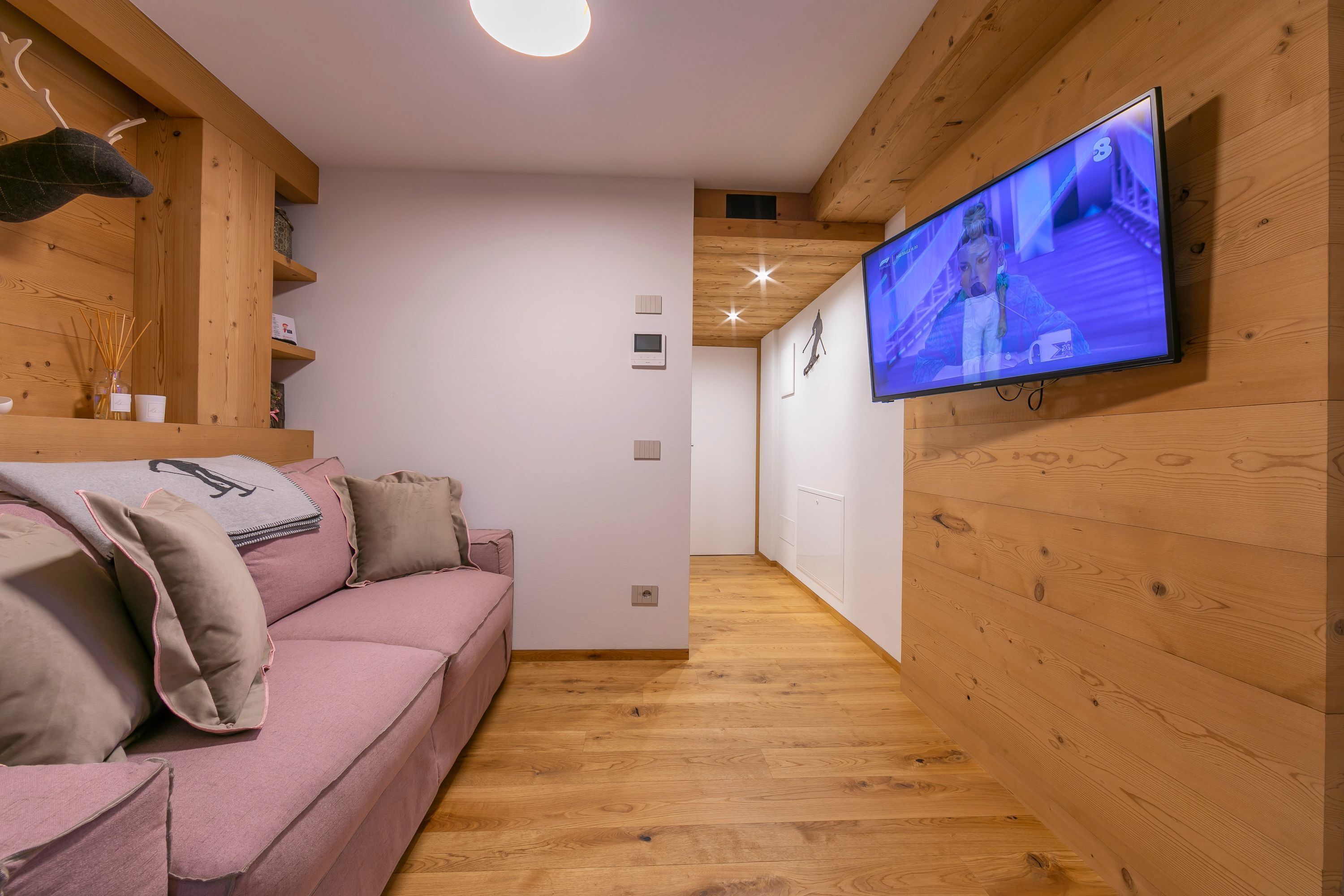 A modern living room with a pink sofa, wooden beams, a mounted TV, and a wooden floor.
