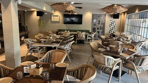 A restaurant with wicker furniture, a flat-screen TV, and a large window. - Origin Boutique Hotel (Arpora)