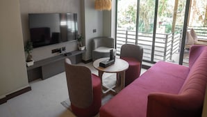 A modern living room with a flat-screen TV, a sofa, two armchairs, a small round table, and a hanging light fixture. - Origin Boutique Hotel (Arpora)