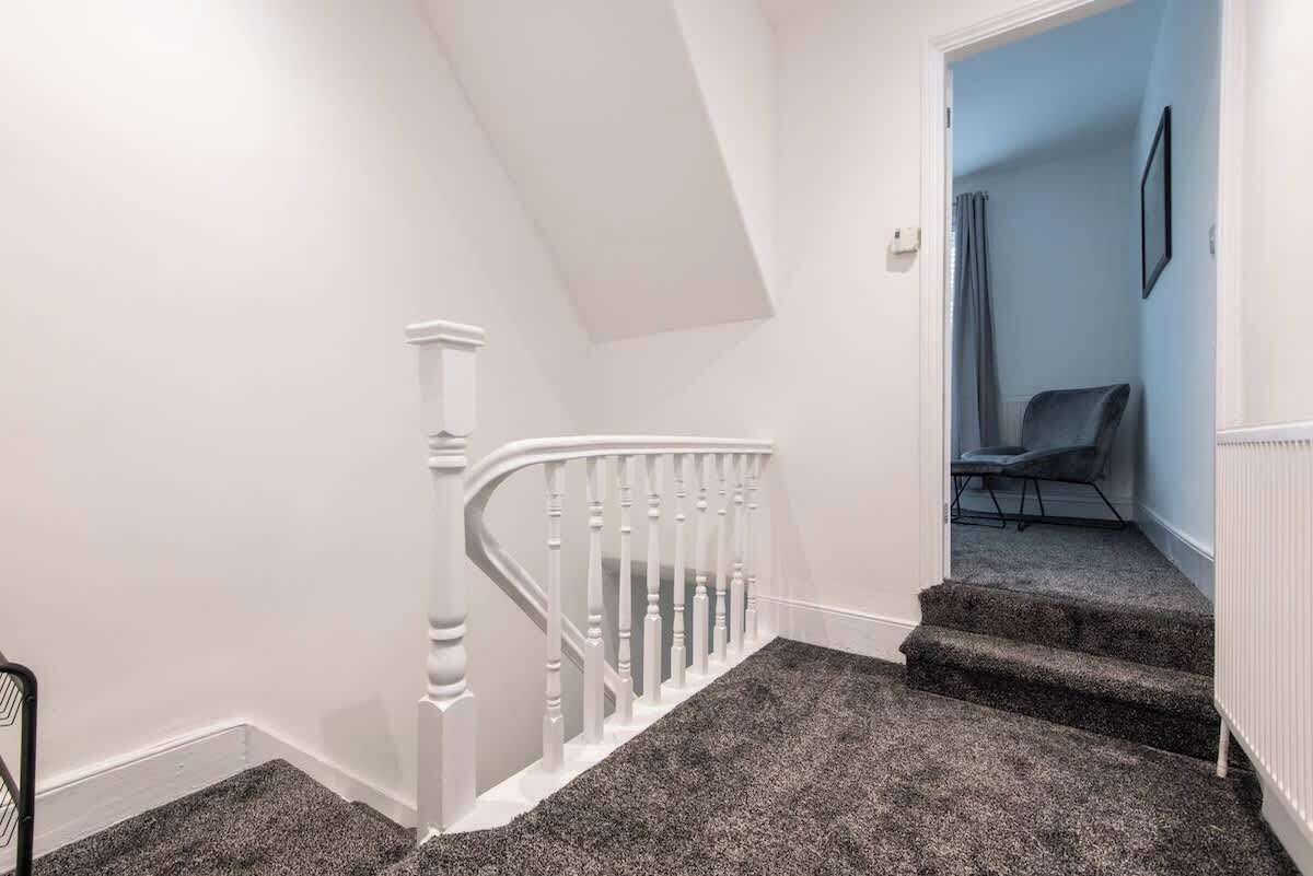 Eine Treppe mit weißer Handläufung, Teppichstufen und einer Tür zu einem Raum mit einem Sessel.