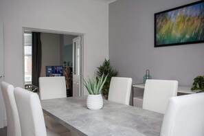 A dining area with a table, chairs, a potted plant, and a painting on the wall.