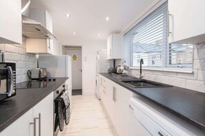 Une cuisine moderne avec des meubles blancs, un plan de travail noir et une fenêtre équipée de stores.