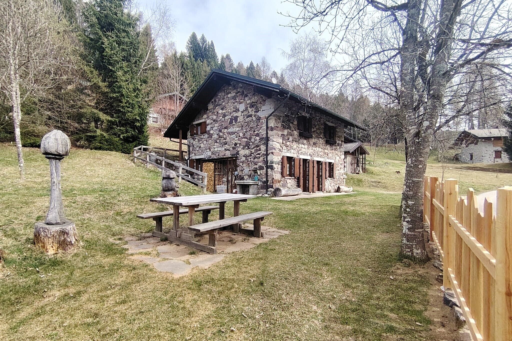 Un bâtiment rustique en pierre, doté d’une terrasse en bois et de tables de pique-nique.