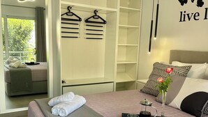 Moderni hotellihuone, jossa on suuri sänky, vaatekaappi, oleskelualue ja näkymä vehreään maisemaan.