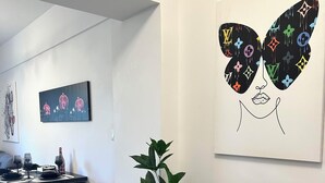 Moderni ruokailutila, jossa on kahdelle katettu pöytä, ruukkukasvi ja seinälle ripustettu taideteos.