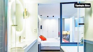 Ein modernes Hotelzimmer mit einem großen Bett, einem separaten Badezimmer und einer Glastür, die auf einen Balkon führt.