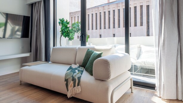 Ein modernes Wohnzimmer mit Sofa, Flachbildfernseher, Topfpflanze und Blick ins Freie.