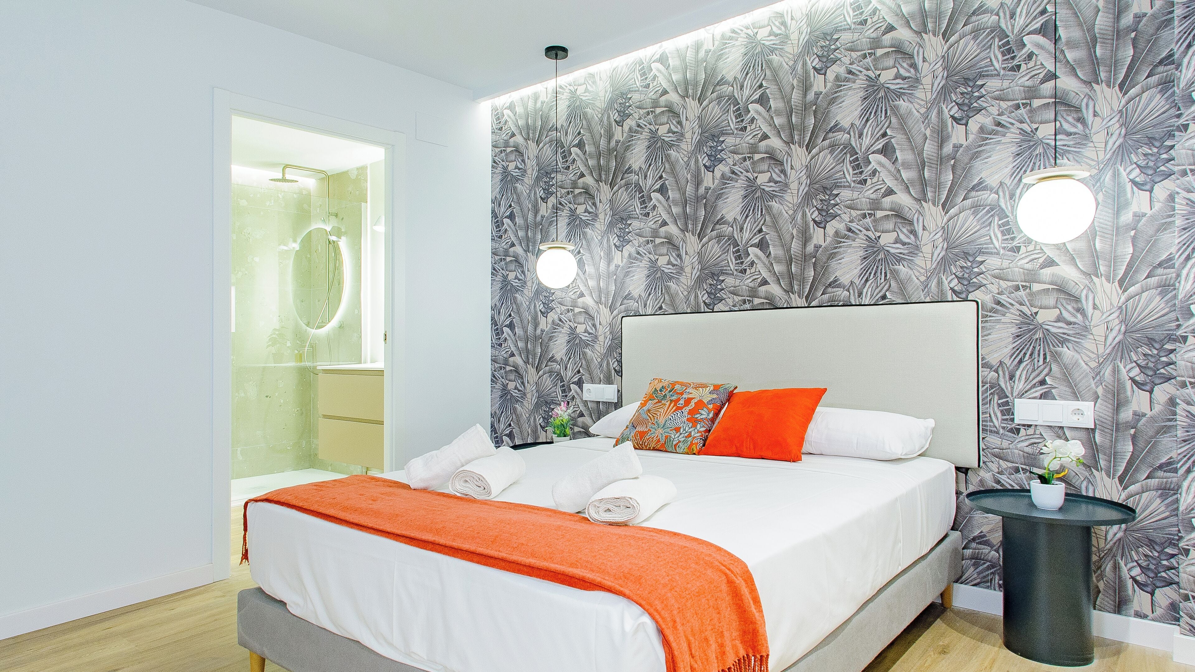 Un dormitorio moderno con una cama grande, una mesita de noche y un baño visible a través de una puerta abierta.