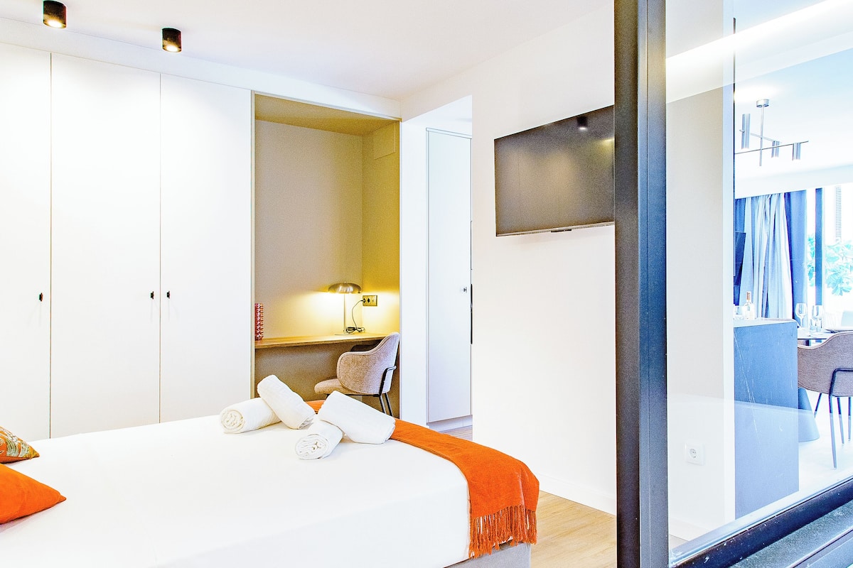 A hotel room with a bed, a desk, a chair, and a view of the outside.