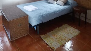 Quarto com cama, mesa de cabeceira de madeira, uma mesinha e janela com cortinas.