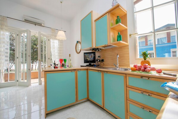 A kitchen with teal cabinets, a wooden countertop, a window with a view, and a door leading to an outdoor area. - Appartamento Bella Vista (Sirmione)