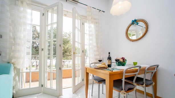 Un comedor con una mesa preparada para dos, una silla, una botella de vino y un jarrón con flores.