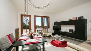 Una sala de estar moderna con comedor, ventanas amplias, un mueble de entretenimiento negro y una alfombra roja.