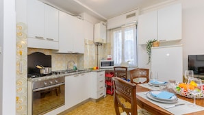 Cocina compacta con armarios blancos, microondas, estufa y comedor con mesa para dos.