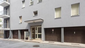 Un edificio moderno con múltiples ventanales, entrada protegida por un portón y zona de estacionamiento.