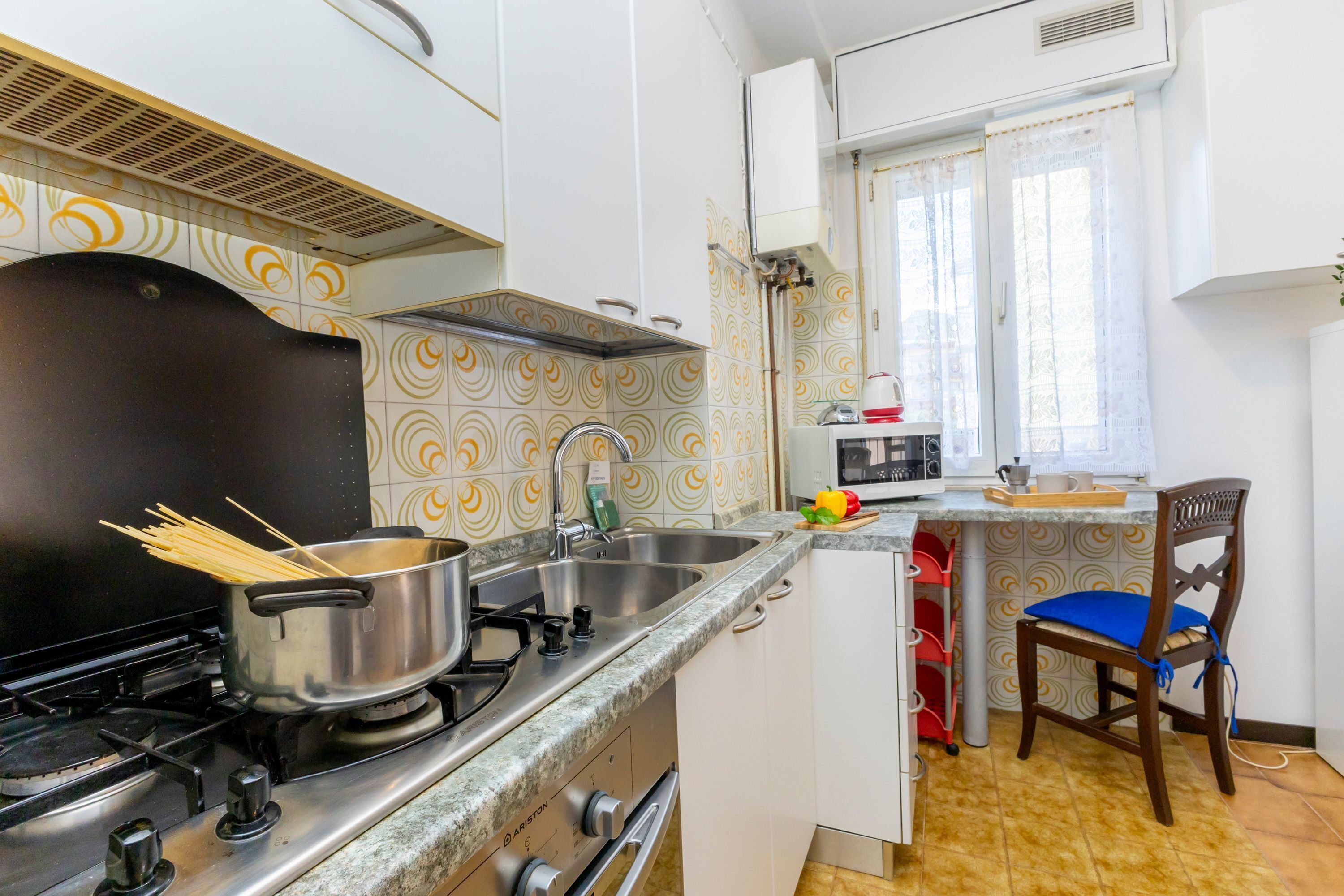 A compact kitchen with a stove, sink, and a small dining area with a chair and table.