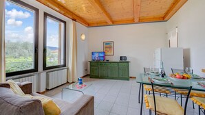 A spacious living area with a wooden ceiling, large windows, a green cabinet, and a dining table set for four.