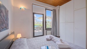 A hotel room with a bed, a nightstand, a lamp, a painting, a wardrobe, and a view of the outdoors.