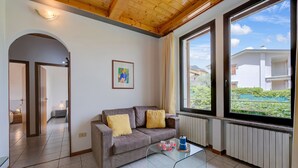 A modern living room with a grey sofa, a glass coffee table, and a large window offering a view of a residential area.