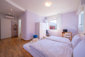A bedroom with two beds, a desk, a chair, a wardrobe, and a window with a view. - Appartamento Bianca Gemma (Riva del Garda)
