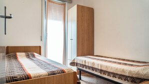 A bedroom with two wooden beds, a wardrobe, and a window with curtains. - Spacious apartment with sea view - Beahost (Bibione)