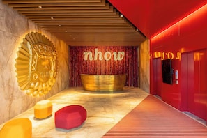 A modern lobby with a reception desk, a large golden sculpture, and a red accent wall.